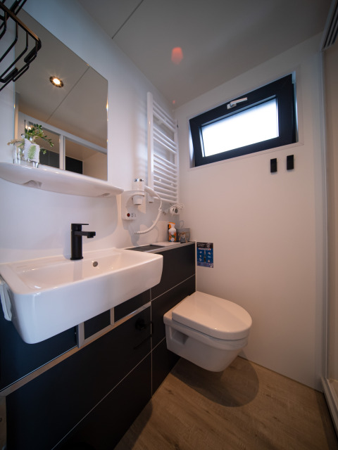 Baño moderno con lavabo, inodoro suspendido y grifería negra en un alojamiento de glamping iluminado.