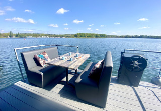 Zona de asientos al aire libre en una casa flotante en Marina Mookerplas, vista al lago y sofás.