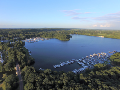 Luchtfoto van een glamping bij een jachthaven aan een meer, omgeven door bomen en groen landschap.