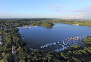 Vista aérea de un sitio glamping junto a un lago y marina, rodeado de árboles y naturaleza verde.