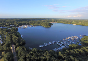 Aerial view of a glamping site by a marina and lake, surrounded by trees and lush green landscape.