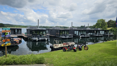 Casa flotante en Marina Mookerplas, Países Bajos, con bicicletas eléctricas y botes frente al césped.