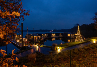 Casa flotante iluminada en Marina Mookerplas, Países Bajos, al anochecer con árbol de Navidad decorado.