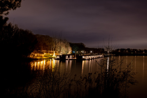 Vue du soir sur Houseboat Marina Mookerplas aux Pays-Bas, avec jetée et lumières sur l'eau calme.
