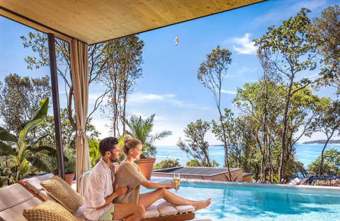 Couple relaxing by the pool at Valamar Camping Istra, overlooking the sea with lush trees in Istria, Croatia.