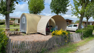 Safari-tent Coco Sweet op een camping met picknicktafel, auto en bomen op een zonnige dag.