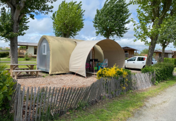 Coco Sweet safaritent op een camping met picknicktafel, wagen en bomen op een zonnige dag.