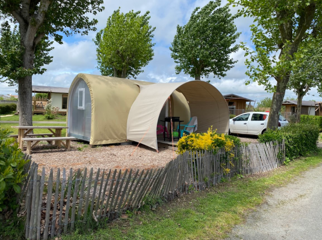Safari-tent Coco Sweet op een camping met picknicktafel, auto en bomen op een zonnige dag.