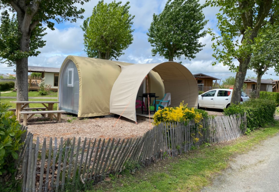 Safari-Zelt Coco Sweet auf einem Campingplatz mit Picknicktisch, Auto und Bäumen bei Sonnenlicht.