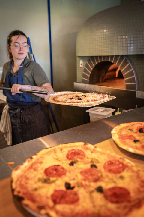 Una mujer hornea pizza en un horno de piedra en Huttopia Caminos de Galicia, parque vacacional en Galicia, España.
