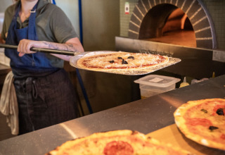 Een vrouw bakt verse pizza in een steenoven bij Huttopia Caminos de Galicia vakantiepark in Galicië, Spanje.