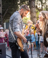 Deux musiciens jouent en plein air devant un public joyeux dans un parc de vacances proposant du glamping.