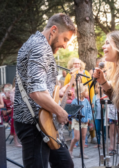 Zwei Musiker treten vor begeistertem Publikum in einem Glamping-Ferienpark im Freien unter Bäumen auf.