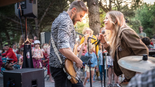 Zwei Musiker treten vor begeistertem Publikum in einem Glamping-Ferienpark im Freien unter Bäumen auf.