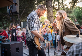 Due musicisti si esibiscono all’aperto davanti a famiglie felici in un parco vacanze con alloggi glamping.