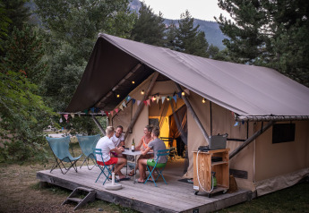 Four people relax on the deck of a Trappeur safari tent, enjoying drinks and conversation in nature.