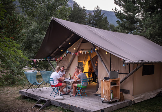 Quattro persone si rilassano sulla veranda di una tenda safari Trappeur, immerse nella natura e nei boschi.