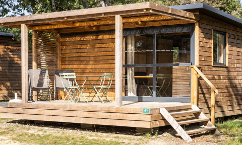 Houten chalet met overdekt terras, tuinstoelen en grote ramen, gefotografeerd bij Chalet Evasion.