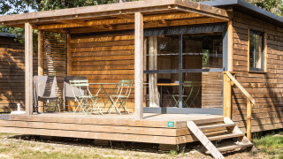Træhytte med overdækket terrasse, havemøbler og store vinduer, omgivet af natur, set ved Chalet Evasion.