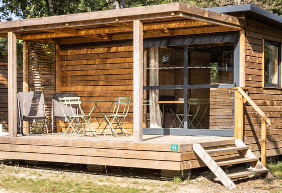 Houten chalet met overdekt terras, tuinstoelen en grote ramen, gefotografeerd bij Chalet Evasion.