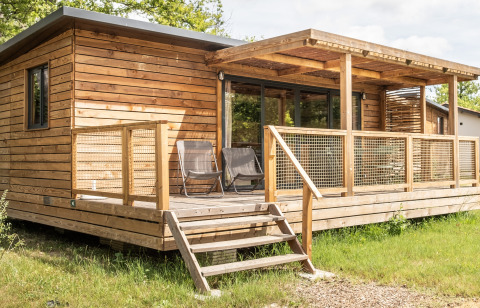 Træhytte med overdækket terrasse og to stole udenfor, fotograferet ved Chalet Portland lodge om sommeren.