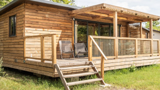Træhytte med overdækket terrasse og to stole udenfor, fotograferet ved Chalet Portland lodge om sommeren.