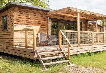 Træhytte med overdækket terrasse og to stole udenfor, fotograferet ved Chalet Portland lodge om sommeren.