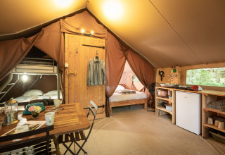 Interno di una tenda safari Trappeur con letto a castello, matrimoniale, zona pranzo e angolo cottura.