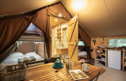 Intérieur d'une tente safari Trappeur confortable avec lits, coin cuisine et table à manger en bois.