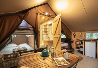 Interior of a cozy Trappeur safari tent featuring beds, a small kitchen area, and a wooden dining table.