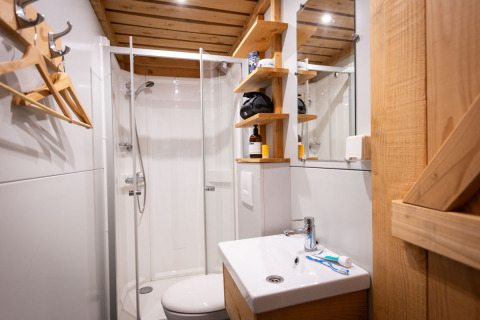 Modern bathroom inside the Trappeur safari tent, featuring a shower, wooden shelves, and a sink.