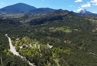 Vista aérea del parque vacacional Huttopia Barcelona Pirineos, rodeado de montañas y bosques en Cataluña, España.