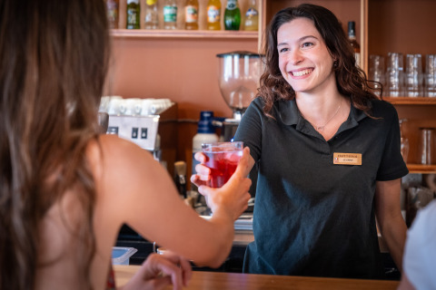 Barmaid souriante à Huttopia Barcelona Pirineos, Catalogne, Espagne, servant une boisson rouge à une cliente.