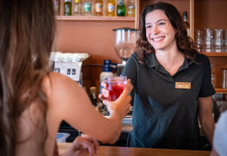 Barista sorridente a Huttopia Barcelona Pirineos, Catalogna, Spagna, serve una bevanda rossa a un ospite.