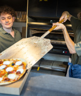 Zwei Männer bereiten Pizza in einer Küche im Ferienpark Huttopia Barcelona Pirineos in Katalonien zu.