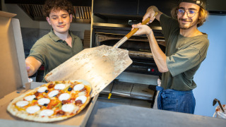Zwei Männer bereiten Pizza in einer Küche im Ferienpark Huttopia Barcelona Pirineos in Katalonien zu.