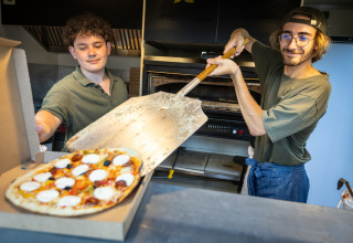 Twee mannen maken pizza in de keuken van Huttopia Barcelona Pirineos vakantiepark in Catalonië, Spanje.