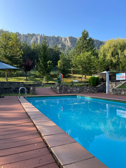 Piscine extérieure avec terrasse en bois, entourée d’arbres et de falaises à Huttopia Barcelona Pirineos, Catalogne.