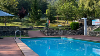 Außenpool mit Holzterrasse und Blick auf grüne Bäume und Felsen im Huttopia Barcelona Pirineos, Katalonien.