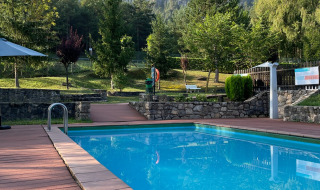 Außenpool mit Holzterrasse und Blick auf grüne Bäume und Felsen im Huttopia Barcelona Pirineos, Katalonien.