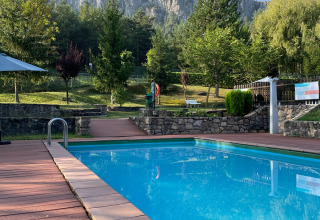Piscina exterior con terraza de madera, rodeada de árboles y acantilados en Huttopia Barcelona Pirineos, Cataluña.