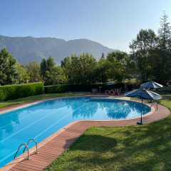 Außenpool mit hölzerner Umrandung, Sonnenschirmen und grüner Landschaft vor Bergkulisse bei gutem Wetter.
