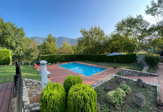 Outdoor pool with wooden deck, lush greenery, and mountain views at Huttopia Barcelona Pirineos, Catalonia.