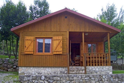 Chalet in legno con base in pietra e veranda anteriore a Huttopia Barcelona Pirineos, immerso nel verde.