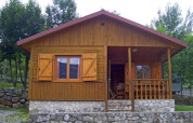 Chalet de madera con base de piedra y porche frontal en Huttopia Barcelona Pirineos, rodeado de árboles.