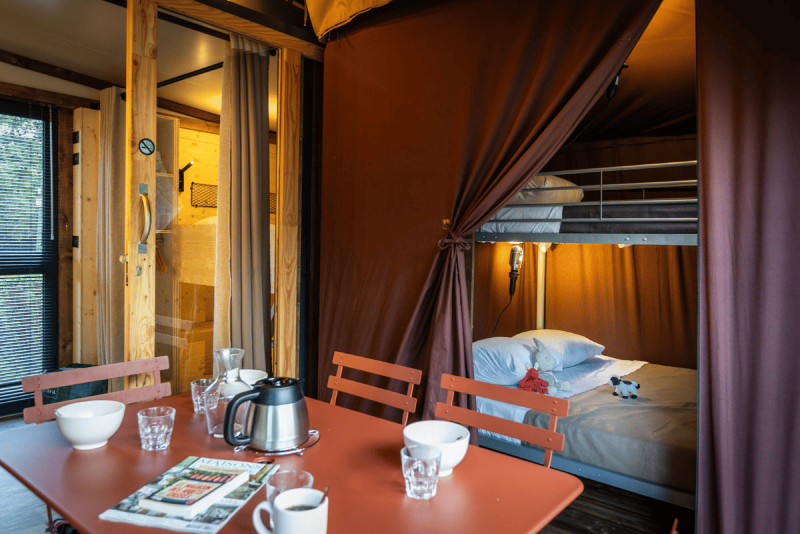 Interieur van glamping Arizona met eettafel, stoelen en een stapelbed achter een gordijn in het verblijf.