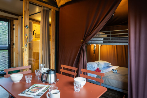 Intérieur de l’hébergement glamping Arizona avec table, chaises et lit superposé derrière un rideau.
