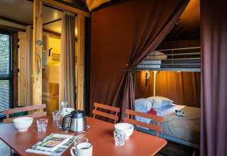 Interior del alojamiento glamping Arizona con mesa de comedor, sillas y litera detrás de una cortina.