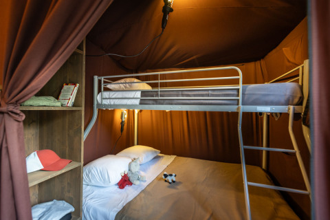 Vue intérieure d'une tente glamping en Arizona avec lits superposés, lumière douce et étagère ouverte.