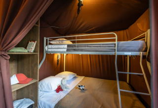 Vue intérieure d'une tente glamping en Arizona avec lits superposés, lumière douce et étagère ouverte.